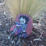 Une petite pirate s’est cachée au pied d’une grande touffe d’herbe dorée. Cherche près des pierres, là où la végétation ressemble à une fontaine sauvage… son trésor rouge n’est pas très loin ! 🏴‍☠️