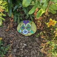 Un mystérieux masque coloré se cache sous les feuillages. Cherche au pied d’un buisson, parmi les copeaux de bois et près des petites fleurs… il veille discrètement dans l’ombre ! 🎭🌿